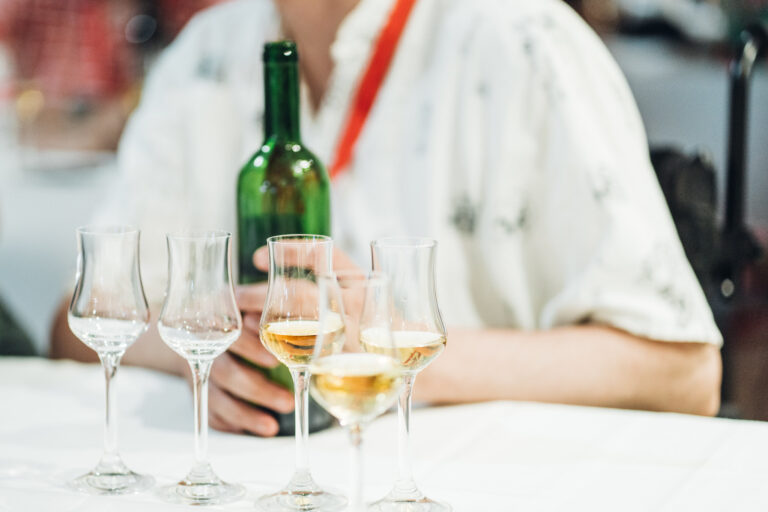 A man holding a bottle on a table. There are glasses filled with spirits in front