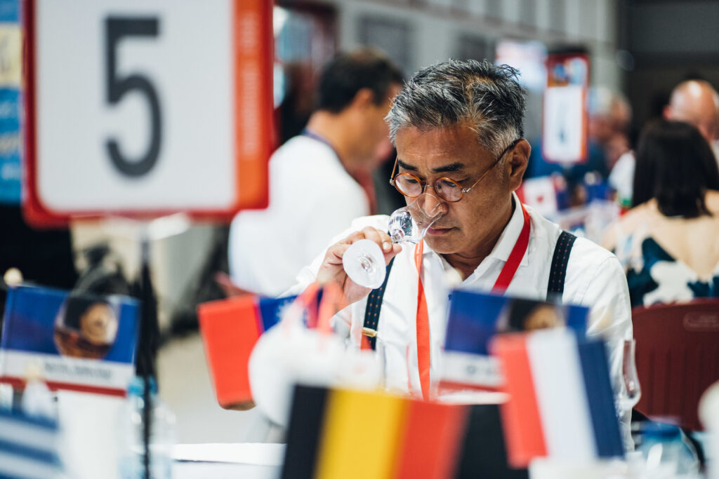 A man with glasses smelling a glass of spirit